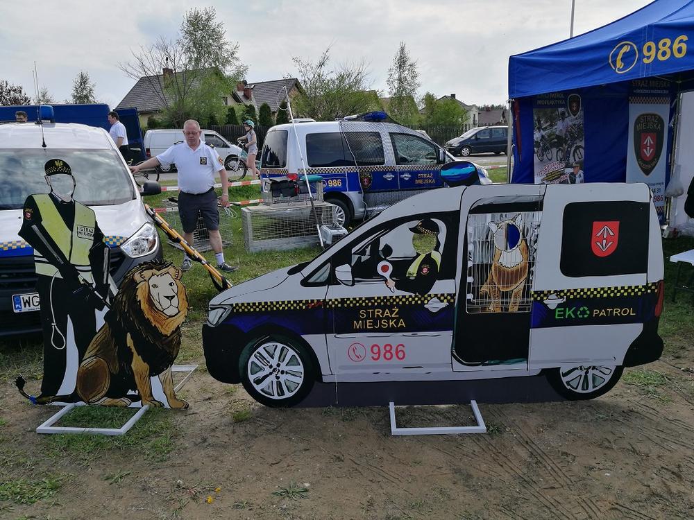 Zdjęcie przedstawiające makiety pojazdu Straży Miejskiej oraz strażnika z psem na imprezie masowej przy namiocie