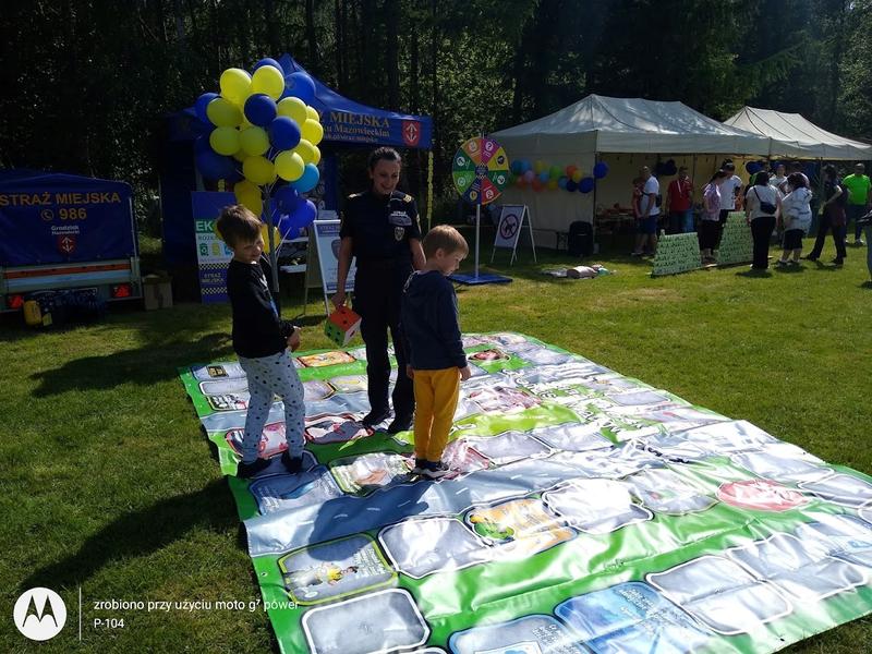 Dzieci bawiące się na makiecie miasteczka ruchu drogowego pod opieką strażniczki Straży Miejskiej