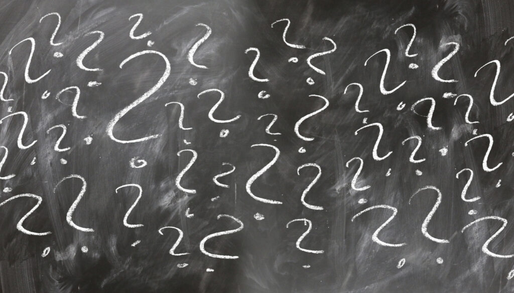 Czarna tablica z wypisanymi na niej kredą pytajnikami